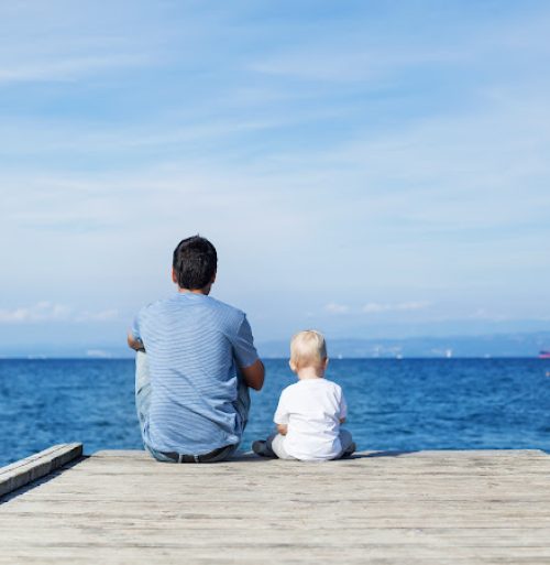 Father with son sitting on the sea pier. Family background. Lifestyle, Holidays and Travel concept. Parent and child together.